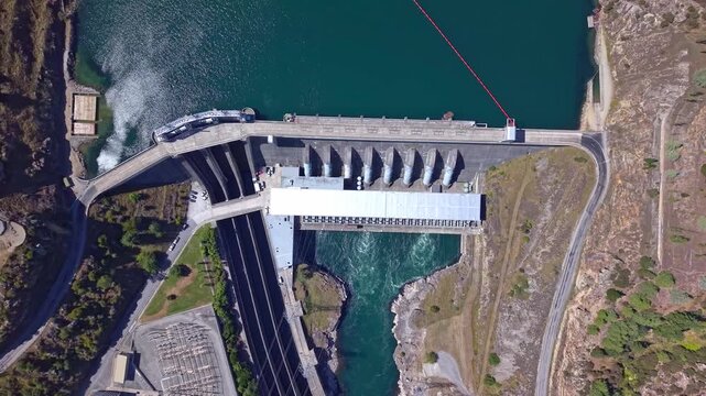 Drone flying in reverse and rising upward, starting from an upper close view of Roxburgh Dam and unzooming to reveal the full hydro structure in Central Otago, New Zealand.