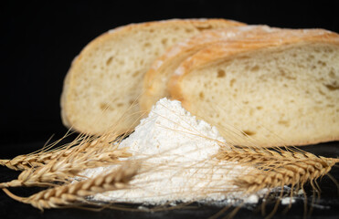 Freshly baked bread with flour and wheat spikes on a dark background showcasing a rustic kitchen setting