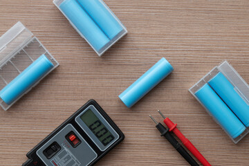 Top view of a multimeter for checking voltage and 18650 lithium-ion battery cells lying on a table.