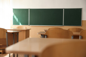 Desks with chairs and green chalkboard in classroom