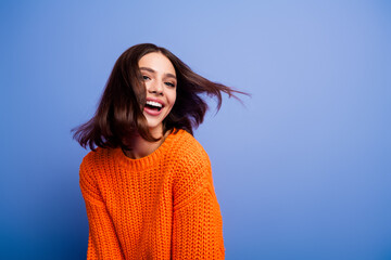 Smiling woman in an orange knit sweater posing against a blue background, showcasing autumn fashion with a playful expression