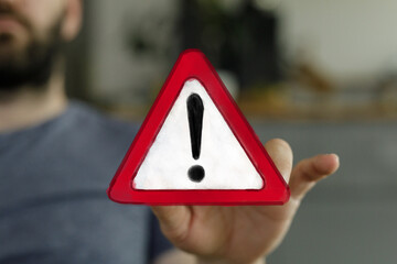Hand holding a red triangle warning sign.  Urgent alert concept.