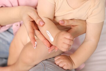 Mother applying cream onto her baby's arm on bed at home, closeup