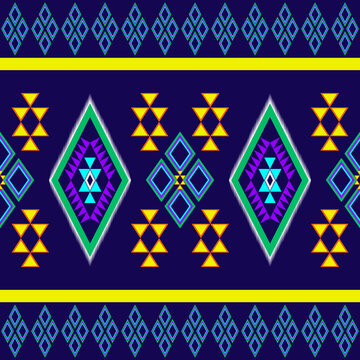 Traditional seamless tribal geometric pattern with colorful diamond and triangle motifs in purple, green, yellow, and orange on a dark navy background. Perfect for textile, fabric, wallpaper, and digi