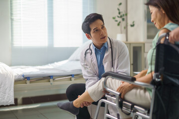 Obraz premium Doctor examining leg of senior patient in wheelchair at hospital