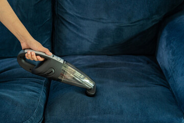 Young maid using handheld cordless vacuum cleaner to vacuuming and cleaning the dust on sofa in home. Housewife using a wireless vacuum machine to cleaner. Housekeeper vacuuming in living room.