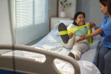 Asian patient doing physiotherapy exercises with resistance band assisted by nurse