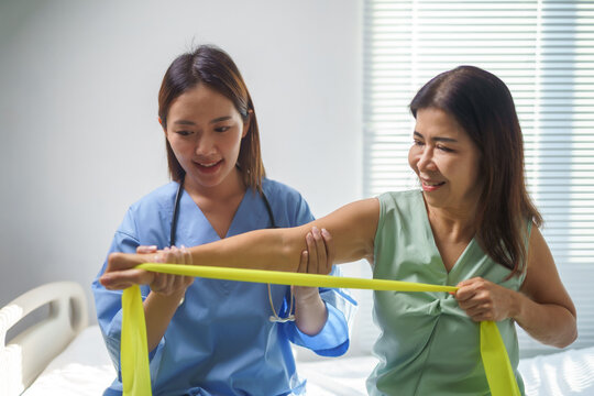 Doctor assisting patient performing exercises with resistance band in hospital room - Powered by Adobe