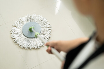Maid using wet mop while cleaning floor at home. Housewife in apron using mop cleaning floor in living room. Housekeeper service worker mopping living room floor and cleaner product to clean dust.