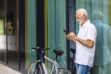 Senior businessman using mobile phone and riding bike in the city.