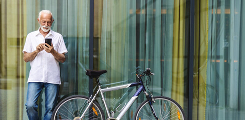 Senior businessman using mobile phone and riding bike in the city.