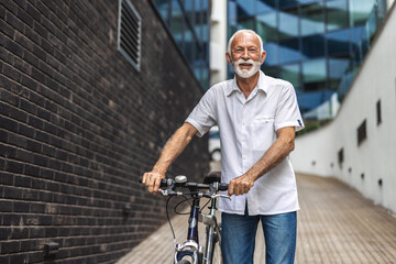 A cheerful senior man pushes his bicycle as he rushes to work. Mature men with commuting to work...