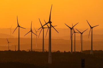 A lot of wind turbines at sunset against the orange sky
