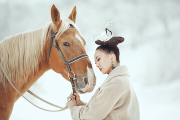 Young stylish asian woman in vintage outfit standing close to a brown horse