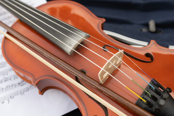 Fototapeta premium Close-up of a beautifully crafted wooden violin resting on sheet music, showcasing intricate details of strings and bridge, evoking a sense of musical artistry and passion for performance