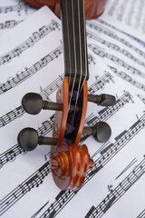 Naklejka premium Close-up view of a wooden violin neck with tuning pegs, resting on a sheet of musical notes, showcasing intricate craftsmanship and the beauty of musical instruments in a creative setting