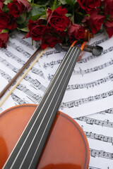 Fototapeta premium Violin resting on sheet music surrounded by vibrant red roses, showcasing a harmonious blend of music and nature, perfect for romantic or artistic themes and celebrations