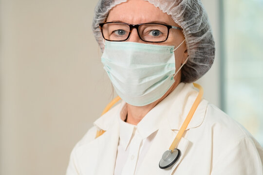 Close-up of senior female doctor in white coat and medical mask. Stethoscope around her neck, she offers expert care and diagnosis in a hospital environment, ensuring patient well-being.