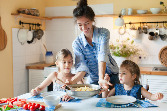 Happy mother serving pasta for daughters at home kitchen. Cozy family lunch, parenthood, comfort food, healthy eating for kids concept. Homemade Italian cuisine, mac and cheese. Authentic lifestyle