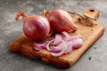 Two whole red onions and slices on a wooden cutting board sit against a gray mottled surface