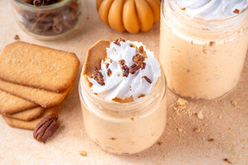 Pumpkin pie overnight oatmeal with whipped cream, nuts and graham crackers. Tasty creamy pumpkin spice oats, on beige background with spice and decorative pumpkins, copy space