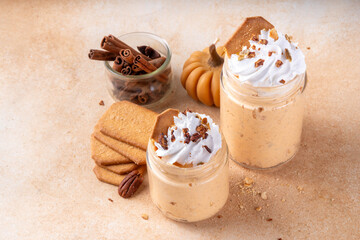 Pumpkin pie overnight oatmeal with whipped cream, nuts and graham crackers. Tasty creamy pumpkin spice oats, on beige background with spice and decorative pumpkins, copy space
