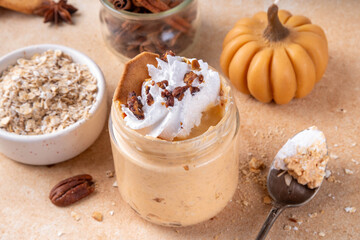 Pumpkin pie overnight oatmeal with whipped cream, nuts and graham crackers. Tasty creamy pumpkin spice oats, on beige background with spice and decorative pumpkins, copy space