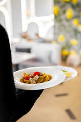Waiter serving pasta with cherry tomatoes and grilled meat in a modern restaurant with lemon-themed decor, showcasing stylish dining and professional food presentation
