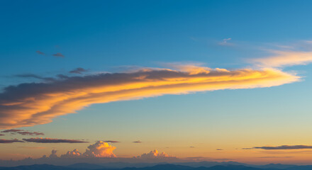 A lenticular cloud formation glows orange during sunset against a blue sky.