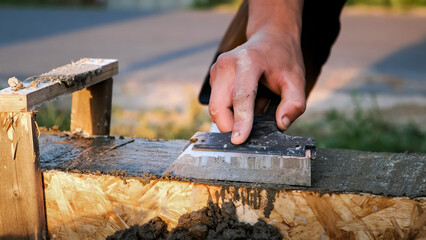 A construction worker smooths wet concrete with trowel in formwork on a building site. Smoothing to create a flat surface. Professional hand work with foundation. High quality photo.