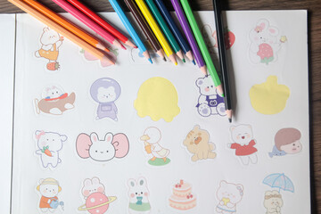 Coloring supplies with vibrant pencils and a sheet of cute cartoon stickers on a wooden desk, symbolizing fun and creativity.