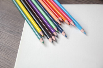 Close-up of a fan of vibrant colored pencils arranged on a plain white sheet of paper on a wooden desk.