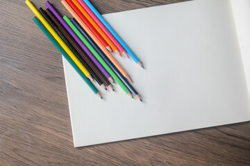 Obraz premium Close-up of a fan of vibrant colored pencils arranged on a plain white sheet of paper on a wooden desk.
