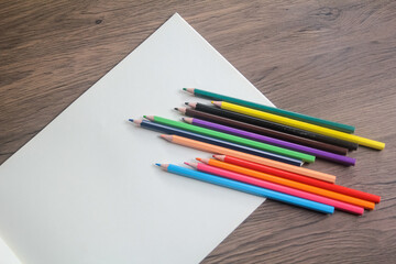Close-up of a fan of vibrant colored pencils arranged on a plain white sheet of paper on a wooden desk.