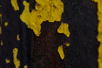Rusty metal surface with peeling yellow paint and dark texture creating an industrial look