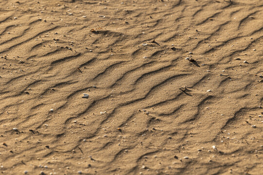 vista macro di una superficie di sabbia di una spiaggia, illuminata dal sole, con onde naturali create dal vento e dalle maree