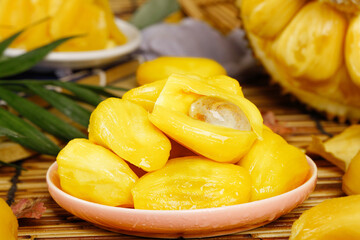 Fresh Yellow Jackfruit Segments in Bowl with Tropical Fruits and Palm Leaves on Wooden Table