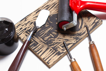 A piece of wooden, black ink, a screen printing roller, spatula and gouges on a white background