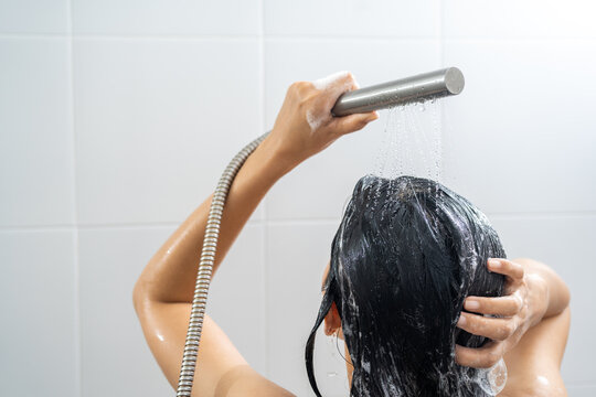Young woman in shower rinse shampoo foaming with water dripping on hair and body. Taking shower relaxing under warm running water. Female washing her hair and hand to massage head while washing hair.