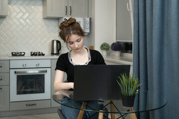 Purposeful young girl working remotely from her kitchen, enjoying a comfortable and convenient workspace while using her laptop. Balancing productivity with modern living in a cozy environment