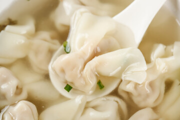 Handmade Wontons in Clear Golden Broth Soup with Green Onions on White Spoon