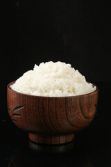 Cooked white rice in wooden bowl on black background - healthy grain food concept