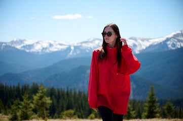 Hiker girl on background of snowy mountains. Young female in red sport jacket and sunglasses hiking in the mountains. Incredible landscape reflects peace and freedom.