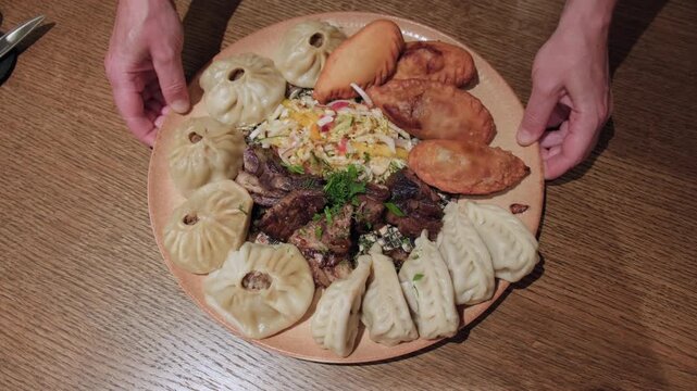 Serving dish of assorted dumplings with fried lamb and salad on plate, top view