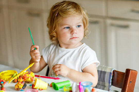 Adorable cute little toddler girl with colorful clay at home. Healthy baby playing and creating toys from play dough at nursery or playschool. Small kid molding modeling clay, creative activity