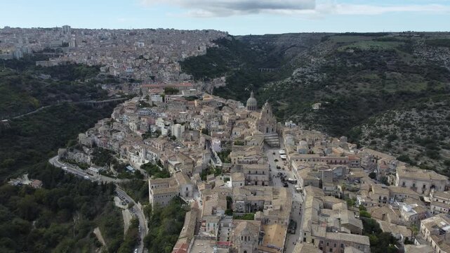 Aerial drone footage of Ragusa in Sicily during the day with clouds, focusing on Duomo di San Giorgio and the historic city center while also showing the wider town and its unique architecture.