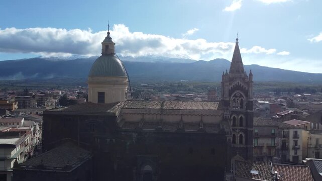 Aerial drone footage of Randazzo in Sicily focusing on the historic center with Basilica di Santa Maria Assunta and the town&rsquo;s medieval architecture, with Mount Etna rising clearly in the background.
