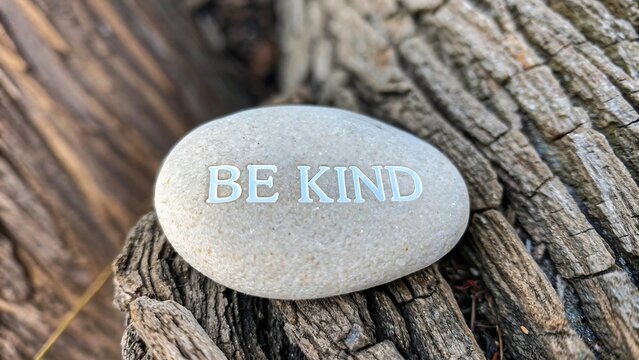 Inspirational stone with BE KIND message placed on tree bark 
 - Powered by Adobe