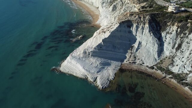 Cinematic 4K drone footage of Scala dei Turchi in Sicily, focusing on the iconic white limestone cliffs, turquoise Mediterranean waters, and the dramatic coastal scenery under bright summer skies.