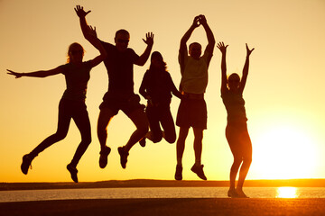 group of young men and women jump together on the beach at sunset on a summer evening